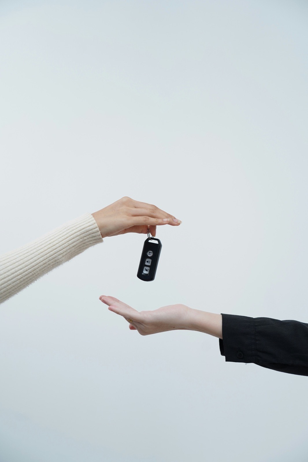 Hands exchanging a car key, representing a completed vehicle purchase.