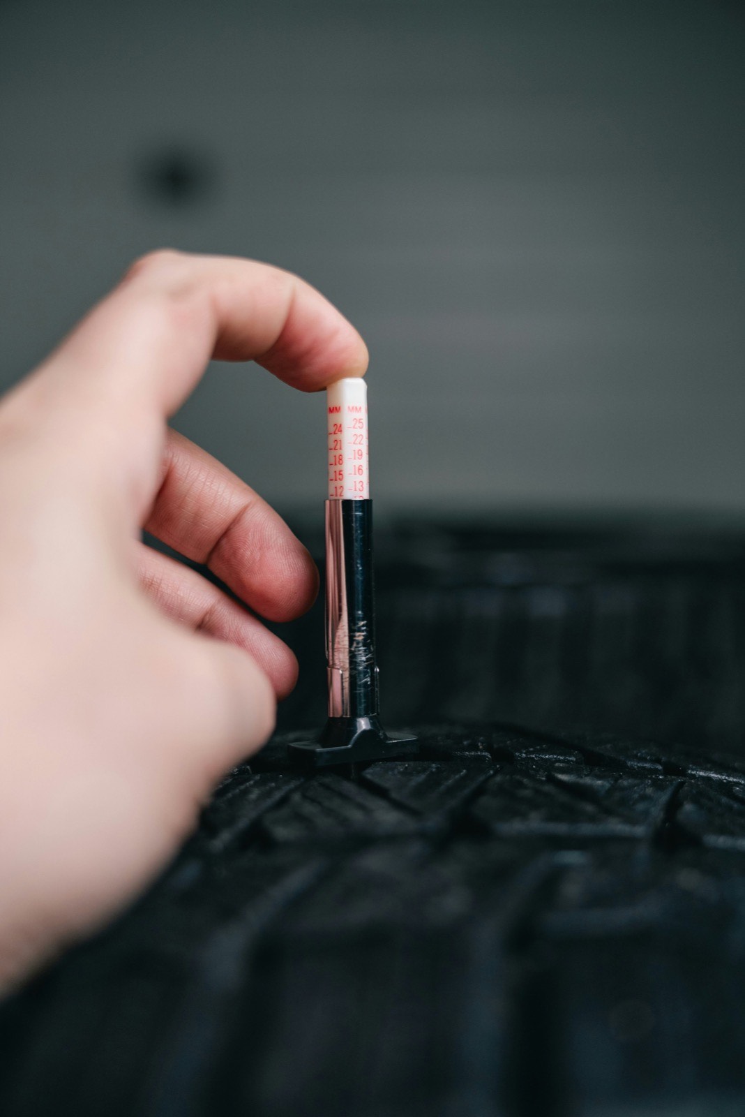 A technician measuring tire tread depth with a gauge as part of a vehicle inspection.